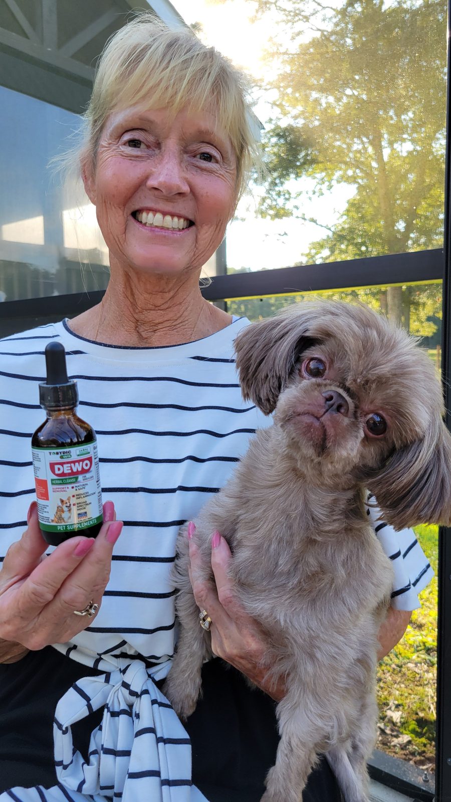 Woman holding a Shih Tzu and a DEWO herbal cleanse dropper bottle